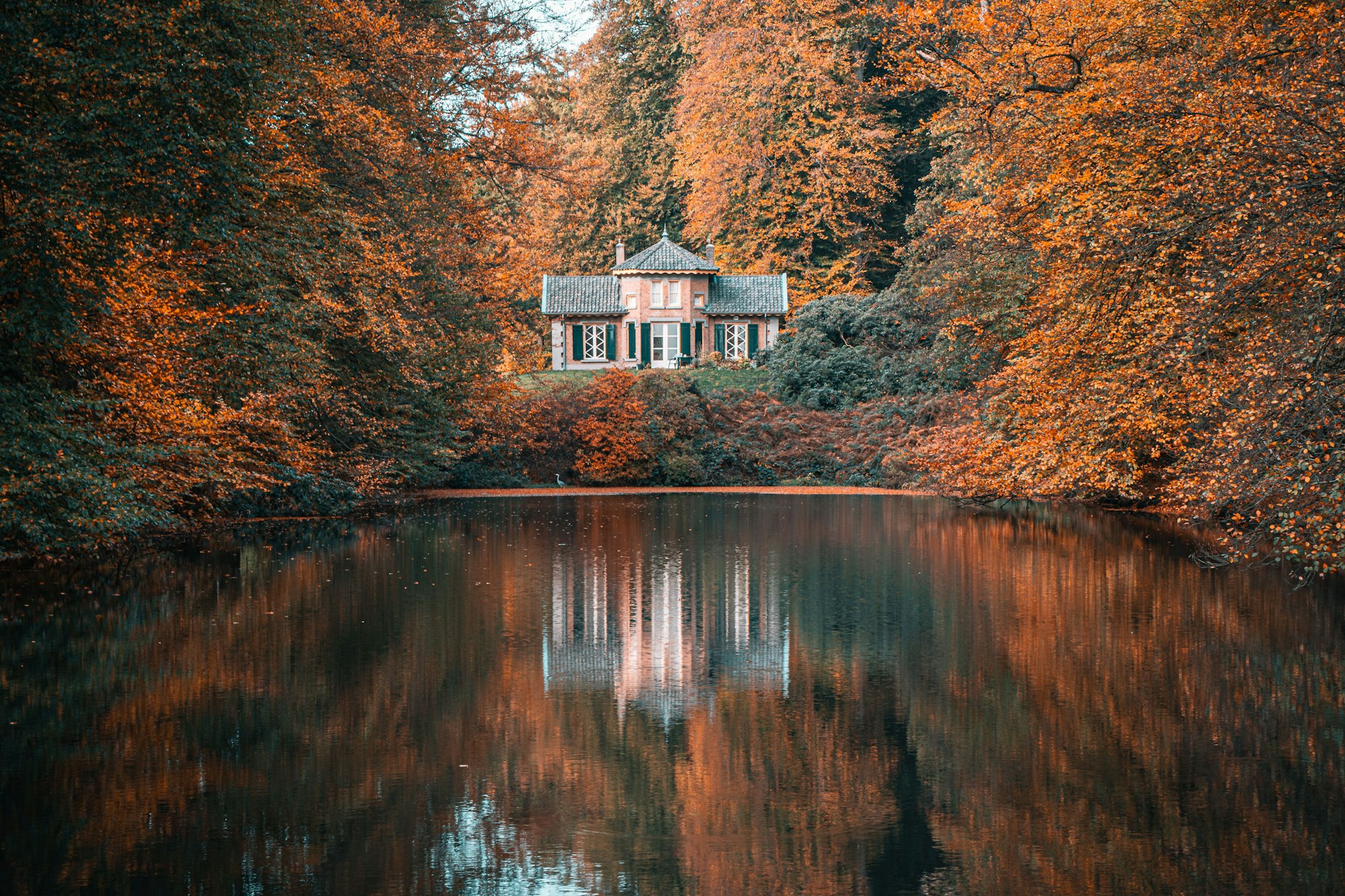 Scenic view of a brick house overlooking a lake surrounded by trees in autumn